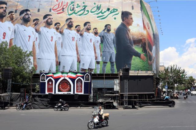 A motorbike is driven past a huge billboard supporting Iran’s national football team in the upcoming 2026 World Cup, installed on a building at Enghelab Square in Tehran on May 18, 2026. Iran's national football team was headed to Turkey on May 18 to play a final friendly match and apply for visas to fly to the United States for the 2026 World Cup, Iranian media reported. (Photo by AFP) / 