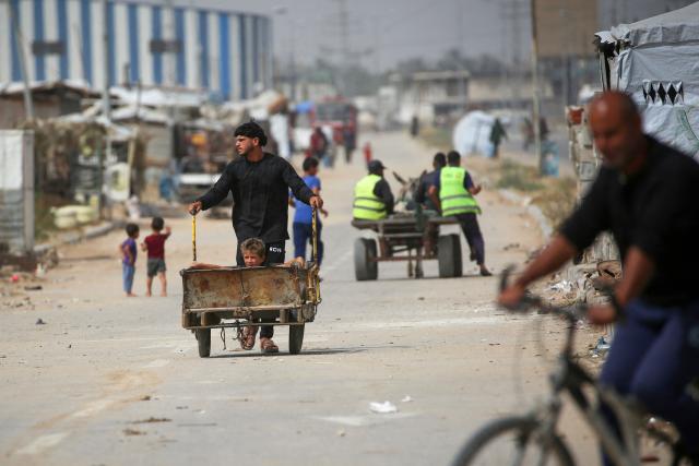 A displaced Palestinian man pushes a trolley with a child sitting in it, as he makes his way past shelters housing hundreds of people whose homes were destroyed in Israeli bombardment, in the Bureij refugee camp in the central Gaza Strip on May 18, 2026. The war has displaced nearly Gaza's entire population and reduced swathes of the Palestinian territory to rubble despite a ceasefire in October 2025, the enclave remains gripped by daily violence as Israeli strikes continue, with both the military and Hamas accusing one another of violating the truce. Hundreds of thousands of people are still living in tents and conditions remain dire despite a ceasefire that took effect in October last year. (Photo by Eyad Baba / AFP)