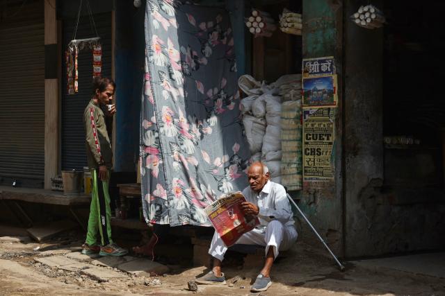 A man drinks tea as another reads a newspaper outside a shop along a street in Varanasi on May 18, 2026. (Photo by Niharika KULKARNI / AFP)