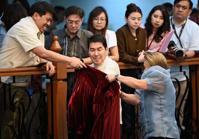 Philippine Senator Erwin Tulfo (C) is helped by staff to put on his robes prior to taking his oath as jurors in the impeachment trial of Vice President Sara Duterte at the plenary hall of the Senate in Manila on May 18, 2026. Philippine lawmakers were sworn in on May 18 to serve as judges in the trial of impeached Vice President Sara Duterte, the second attempt since last year to force her from office. (Photo by Ted ALJIBE / AFP)