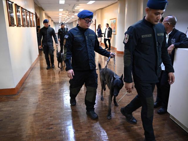 Police officers and their sniffing dogs walk along a hallway after inspecting the plenary hall before the Philippine senators took their oath as jurors in the impeachment trial of Vice President Sara Duterte at the Senate in Manila on May 18, 2026. Philippine lawmakers were sworn in on May 18 to serve as judges in the trial of impeached Vice President Sara Duterte, the second attempt since last year to force her from office. (Photo by Ted ALJIBE / AFP)
