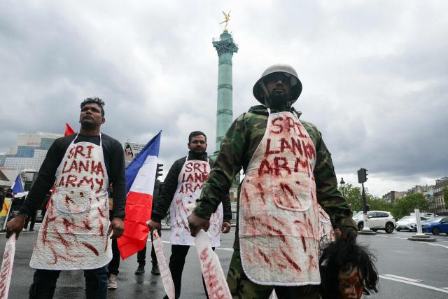 Members of the Tamil community in France wearing fake blood-stained aprons bearing the words “Sri Lankan Army” stage a protest at Place de la Bastille in Paris on May 18, 2026, demanding that Sri Lanka recognize what they describe as the Tamil genocide. (Photo by Alain JOCARD / AFP)