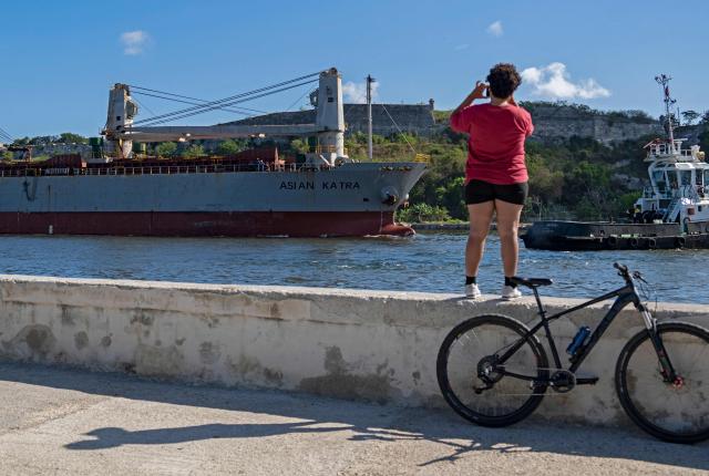 A woman takes photographs of the Asian Katra, a Panama-flagged cargo ship, as it arrives in Havana Bay carrying humanitarian aid, in Havana, Cuba, on May 18, 2026. A new shipment of humanitarian aid from Mexico arrived in Cuba on May 18, as the island grapples with a severe economic and energy crisis nearly four months after the imposition of an oil blockade by Washington. (Photo by YAMIL LAGE / AFP)
