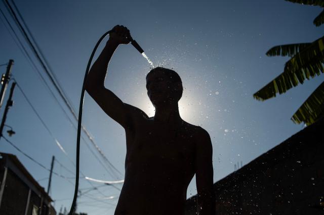 (FILES) A man cools off with a hose on the street amid a heat wave in the Guaratiba neighborhood of Rio de Janeiro, Brazil, on February 17, 2025. Heat waves and other extreme weather ravaged Latin America and the Caribbean in 2025, but tallying the death toll from these events is a near-impossible task, a report published by the World Meteorological Organization (WMO) in Brasilia on May 18, 2026, warned. (Photo by TERCIO TEIXEIRA / AFP)