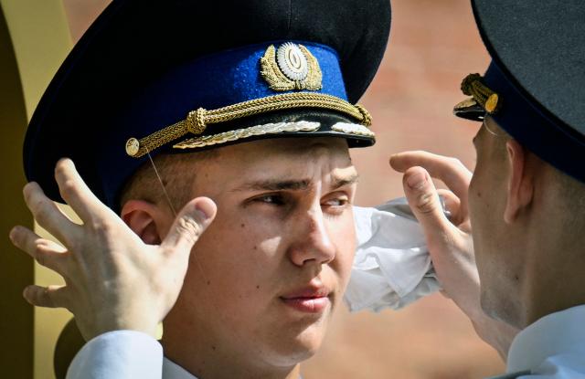 A Russian honour guard soldier adjusts his soldier mate's cap and wipes off sweat while his colleague stands guard at the Tomb of the Unknown Soldier in downtown Moscow on May 18, 2026, as the temperature raised up to 30 centigrade. (Photo by Alexander NEMENOV / AFP)