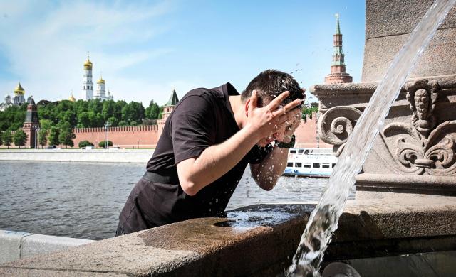 A man refreshes himself in a small fountain, with the Kremlin seen in distance, in downtown Moscow on May 18, 2026, as the temperature raised up to 30 centigrade. (Photo by Alexander NEMENOV / AFP)