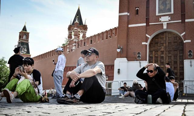 Tourists hide themselves in the shadow of the Spasskaya tower of the Kremlin in downtown Moscow on May 18, 2026, as the temperature raised up to 30 centigrade. (Photo by Alexander NEMENOV / AFP)