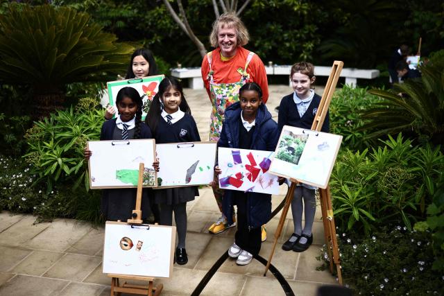 British artist Grayson Perry poses with children from a local primary school in the Tate Britain Garden on the press day ahead of the 2026 RHS Chelsea Flower Show in London on May 18, 2026. Emphasising nature's power to protect, a giant fallen tree in one garden has been carved into a sculpture of a sleeping guardian, Gaia, or Mother Nature. "The garden aims to bring to you the potential and the joy in the ordinary," said Sarah Eberle, designer of the Garden on the Edge from the Campaign for Protection of Rural England. (Photo by Henry NICHOLLS / AFP)