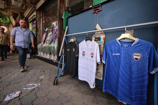 A man walks past football jerseys bearing the Iraqi national flag displayed at a sportswear shop in Baghdad on May 18, 2026, ahead of the 2026 FIFA World Cup, for which the country qualified. The "Lions of Mesopotamia" secured the country's first World Cup appearance since the 1986 competition in Mexico with a 2-1 win over Bolivia on March 31, 2026. (Photo by AHMAD AL-RUBAYE / AFP)