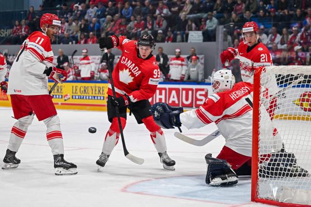 Canada’s forward #93 Fraser Minten tries to control the puck next to Denmark's forward #11 Alexander True and Denmark's goalkeeper #1 Nicolaj Henriksen during the groupe B match between Canada and Denmark at the IIHF Ice Hockey Men's World Championship at BFC Arena, in Fribourg, Switzerland, on May 18, 2026. (Photo by Fabrice COFFRINI / AFP)