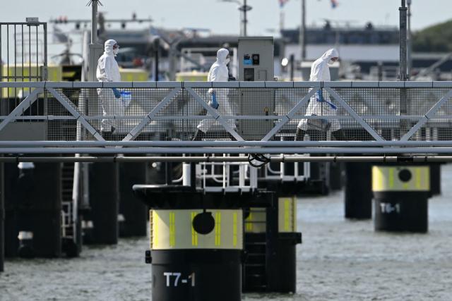 Persons in protective hazmat suits leave after inspecting the Dutch Hantavirus-hit cruise ship MV Hondius as it arrived at the port of Rotterdam on May 18, 2026. A cruise ship that sparked global alarm after a deadly outbreak of hantavirus docked in Rotterdam harbour on May 18, with the skeleton crew facing weeks of quarantine. (Photo by NICOLAS TUCAT / AFP)