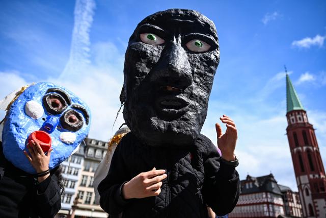Participants wearing masks gestures during a rally in support of student theatres on the central Roemer Square in Frankfurt am Main, western Germany, on May 18, 2026. (Photo by Kirill KUDRYAVTSEV / AFP)