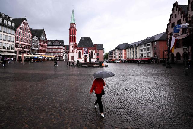 A woman shelters under an umbrella against light rain as she walks along on the central Roemer Square in Frankfurt am Main, western Germany, on May 18, 2026 with air temperature reaching 16 degrees Celsius. (Photo by Kirill KUDRYAVTSEV / AFP)
