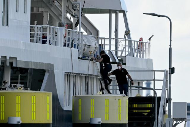 A masked crew member helps another crew member disembarks from the Dutch Hantavirus-hit cruise ship MV Hondius docked at the port of Rotterdam on May 18, 2026. A cruise ship that sparked global alarm after a deadly outbreak of hantavirus docked in Rotterdam harbour on May 18, with the skeleton crew facing weeks of quarantine. (Photo by NICOLAS TUCAT / AFP)