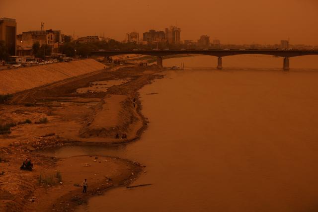 People stand on the banks of the Tigris River in central Baghdad on May 18, 2026, during a dust storm coming from western Iraq. (Photo by AHMAD AL-RUBAYE / AFP)
