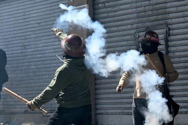 A miner throws a tear gas canister back at riot police during a protest demanding the resignation of Bolivian President Rodrigo Paz, in La Paz, on May 18, 2026. Bolivians have taken to the streets for the past two weeks, blocking roads into La Paz and disrupting deliveries of food, medicine and other goods to the seat of government, while demanding higher wages, economic relief and the resignation of centre-right President Rodrigo Paz amid a severe economic crisis. (Photo by AIZAR RALDES / AFP)