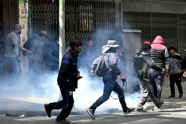 Protesters run to escape tear gas during clashes with riot police in a protest demanding the resignation of Bolivian President Rodrigo Paz, in La Paz, on May 18, 2026. Bolivians have taken to the streets for the past two weeks, blocking roads into La Paz and disrupting deliveries of food, medicine and other goods to the seat of government, while demanding higher wages, economic relief and the resignation of centre-right President Rodrigo Paz amid a severe economic crisis. (Photo by AIZAR RALDES / AFP)