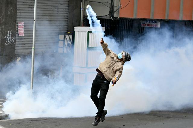 A miner throws a tear gas canister back at riot police during a protest demanding the resignation of Bolivian President Rodrigo Paz, in La Paz, on May 18, 2026. Bolivians have taken to the streets for the past two weeks, blocking roads into La Paz and disrupting deliveries of food, medicine and other goods to the seat of government, while demanding higher wages, economic relief and the resignation of centre-right President Rodrigo Paz amid a severe economic crisis. (Photo by AIZAR RALDES / AFP)