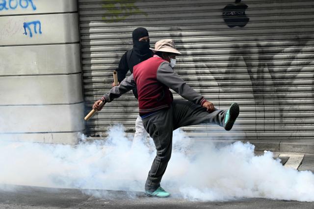 A miner kicks away a tear gas canister thrown by riot police during a protest demanding the resignation of Bolivian President Rodrigo Paz, in La Paz, on May 18, 2026. Bolivians have taken to the streets for the past two weeks, blocking roads into La Paz and disrupting deliveries of food, medicine and other goods to the seat of government, while demanding higher wages, economic relief and the resignation of centre-right President Rodrigo Paz amid a severe economic crisis. (Photo by AIZAR RALDES / AFP)