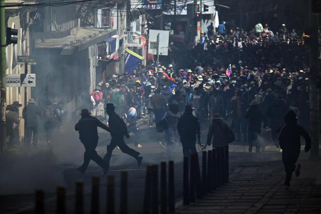 Protesters run to escape tear gas during clashes with riot police in a protest demanding the resignation of Bolivian President Rodrigo Paz, in La Paz, on May 18, 2026. Bolivians have taken to the streets for the past two weeks, blocking roads into La Paz and disrupting deliveries of food, medicine and other goods to the seat of government, while demanding higher wages, economic relief and the resignation of centre-right President Rodrigo Paz amid a severe economic crisis. (Photo by AIZAR RALDES / AFP)