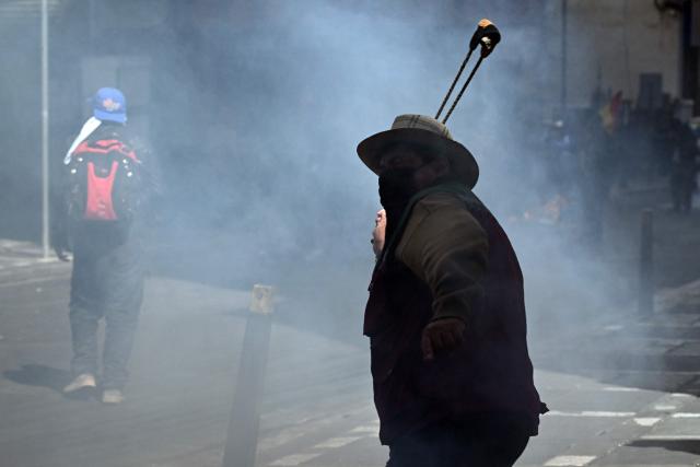 A demonstrator uses a sling ring to throw a stone at riot police during a protest to demand the resignation of Bolivia's President Rodrigo Paz in La Paz, on May 18, 2026. Bolivians have taken to the streets for the past two weeks, blocking roads into La Paz and disrupting deliveries of food, medicine and other goods to the seat of government, while demanding higher wages, economic relief and the resignation of centre-right President Rodrigo Paz amid a severe economic crisis (Photo by AIZAR RALDES / AFP)