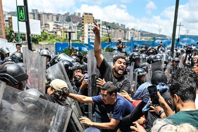 Students of the Central University of Venezuela (UCV) scuffle with a Bolivarian National Police (PNB) officer during a protest following the death of Carmen Navas, the mother of late political prisoner Victor Quero Navas, in Caracas, on May 18, 2026. The mother of Venezuelan political prisoner Victor Hugo Quero Navas died on May 17, 2026 at age 81, just days after confirming the death of her son in state custody, her relatives told AFP. (Photo by Juan BARRETO / AFP)