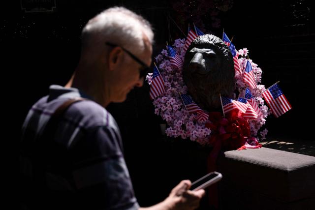 A man passes a lion statue with US flags around its neck in Washington, DC, on May 18, 2026. (Photo by Brendan Smialowski / AFP)