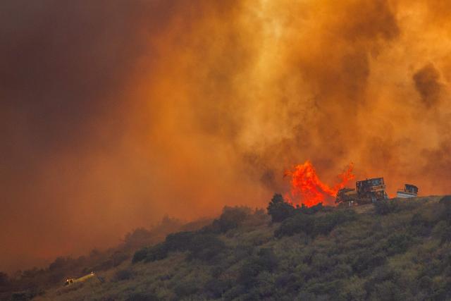 Fire fighters use a bulldozer to combat the Sandy Fire as it burns on a hill at a residential area in Simi Valley, California, on May 18, 2026. About 24,000 people in Simi Valley, 40 miles northwest of Los Angeles, are under mandatory evacuation orders as the Sandy Fire is "spreading dangerously fast" according to fire officials. (Photo by Apu GOMES / AFP)