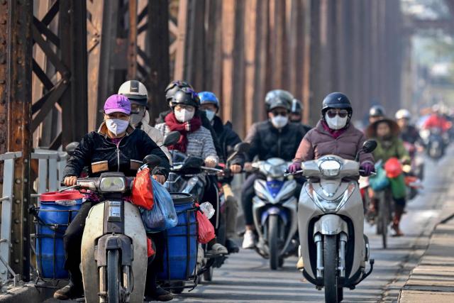 (FILES) Motorists wearing face masks ride motorbikes and scooters along Long Bien Bridge amid heavy air pollution in Hanoi on January 3, 2025. Millions of exhaust-belching motorbikes zip through Hanoi's narrow streets every day fuelling its chronic air pollution, but authorities have backtracked from an ambitious plan to ban them in favour of electric two-wheelers. (Photo by Nhac NGUYEN / AFP) / To go with 'VIETNAM-CLIMATE-POLLUTION-TRANSPORT,FOCUS' by Tran Thi Minh Ha and Lam Nguyen)