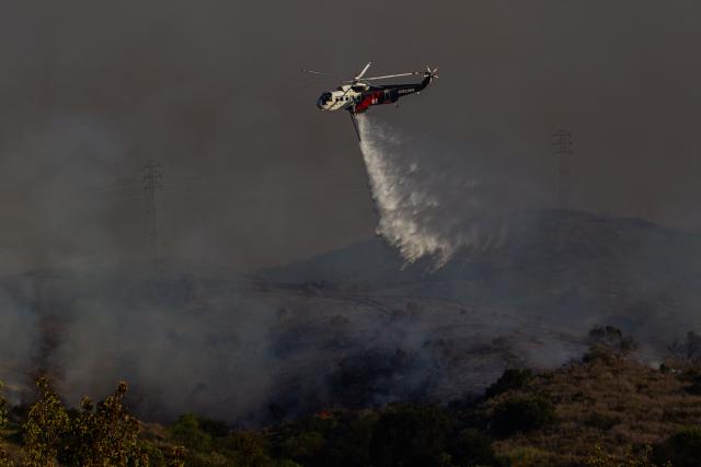 CORRECTION / A Fire Department helicopter drops water on the Sandy Fire as it burns in the hills near a residential area in Simi Valley, California on May 18, 2026. A brush fire broke out May 15 in the suburbs of Los Angeles, spreading rapidly and prompting authorities to issue evacuation orders for thousands of residents. Dubbed the Sandy Fire, the blaze broke out late morning in Simi Valley, a city of roughly 125,000 residents about 40 miles (60 kilometers) northwest of downtown Los Angeles. (Photo by Apu GOMES / AFP) / The erroneous mention[s] appearing in the metadata of this photo by Apu GOMES has been modified in AFP systems in the following manner: [May 18] instead of [May 15]. Please immediately remove the erroneous mention[s] from all your online services and delete it (them) from your servers. If you have been authorized by AFP to distribute it (them) to third parties, please ensure that the same actions are carried out by them. Failure to promptly comply with these instructions will entail liability on your part for any continued or post notification usage. Therefore we thank you very much for all your attention and prompt action. We are sorry for the inconvenience this notification may cause and remain at your disposal for any further information you may require.