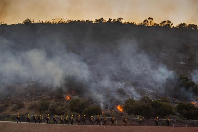 CORRECTION / Firefighters walk by a burning hillside as the Sandy Fire threatens a residential area in Simi Valley, California on May 18, 2026. A brush fire broke out May 15 in the suburbs of Los Angeles, spreading rapidly and prompting authorities to issue evacuation orders for thousands of residents. Dubbed the Sandy Fire, the blaze broke out late morning in Simi Valley, a city of roughly 125,000 residents about 40 miles (60 kilometers) northwest of downtown Los Angeles. (Photo by Apu GOMES / AFP) / The erroneous mention[s] appearing in the metadata of this photo by Apu GOMES has been modified in AFP systems in the following manner: [May 18] instead of [May 15]. Please immediately remove the erroneous mention[s] from all your online services and delete it (them) from your servers. If you have been authorized by AFP to distribute it (them) to third parties, please ensure that the same actions are carried out by them. Failure to promptly comply with these instructions will entail liability on your part for any continued or post notification usage. Therefore we thank you very much for all your attention and prompt action. We are sorry for the inconvenience this notification may cause and remain at your disposal for any further information you may require.