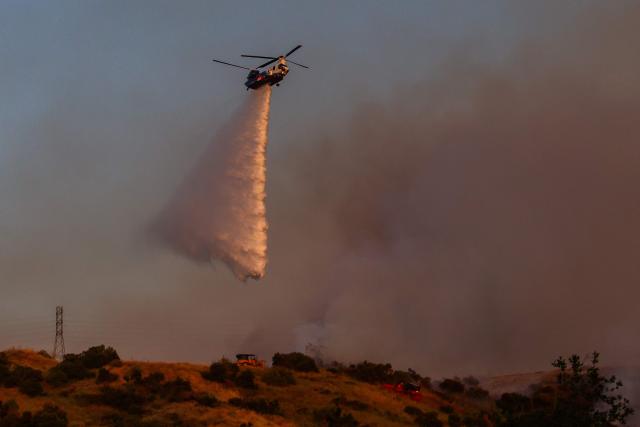 CORRECTION / A Fire Department helicopter drops water on the Sandy Fire as it burns in the hills near a residential area in Simi Valley, California on May 18, 2026. A brush fire broke out May 15 in the suburbs of Los Angeles, spreading rapidly and prompting authorities to issue evacuation orders for thousands of residents. Dubbed the Sandy Fire, the blaze broke out late morning in Simi Valley, a city of roughly 125,000 residents about 40 miles (60 kilometers) northwest of downtown Los Angeles. (Photo by Apu GOMES / AFP) / The erroneous mention[s] appearing in the metadata of this photo by Apu GOMES has been modified in AFP systems in the following manner: [May 18] instead of [May 15]. Please immediately remove the erroneous mention[s] from all your online services and delete it (them) from your servers. If you have been authorized by AFP to distribute it (them) to third parties, please ensure that the same actions are carried out by them. Failure to promptly comply with these instructions will entail liability on your part for any continued or post notification usage. Therefore we thank you very much for all your attention and prompt action. We are sorry for the inconvenience this notification may cause and remain at your disposal for any further information you may require.