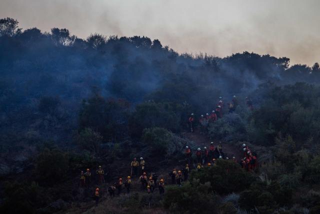 CORRECTION / Firefighters and inmate firefighters walk through a scorched hillside as they fight the Sandy Fire in Simi Valley, California on May 18, 2026. A brush fire broke out May 15 in the suburbs of Los Angeles, spreading rapidly and prompting authorities to issue evacuation orders for thousands of residents. Dubbed the Sandy Fire, the blaze broke out late morning in Simi Valley, a city of roughly 125,000 residents about 40 miles (60 kilometers) northwest of downtown Los Angeles. (Photo by Apu GOMES / AFP) / The erroneous mention[s] appearing in the metadata of this photo by Apu GOMES has been modified in AFP systems in the following manner: [May 18] instead of [May 15]. Please immediately remove the erroneous mention[s] from all your online services and delete it (them) from your servers. If you have been authorized by AFP to distribute it (them) to third parties, please ensure that the same actions are carried out by them. Failure to promptly comply with these instructions will entail liability on your part for any continued or post notification usage. Therefore we thank you very much for all your attention and prompt action. We are sorry for the inconvenience this notification may cause and remain at your disposal for any further information you may require.
