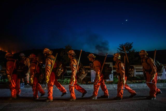 Inmate firefighters walk back to their fire truck after combating the Sandy Fire in Simi Valley, California on May 18, 2026. A brush fire broke out May 15 in the suburbs of Los Angeles, spreading rapidly and prompting authorities to issue evacuation orders for thousands of residents. Dubbed the Sandy Fire, the blaze broke out late morning in Simi Valley, a city of roughly 125,000 residents about 40 miles (60 kilometers) northwest of downtown Los Angeles. (Photo by Apu GOMES / AFP)