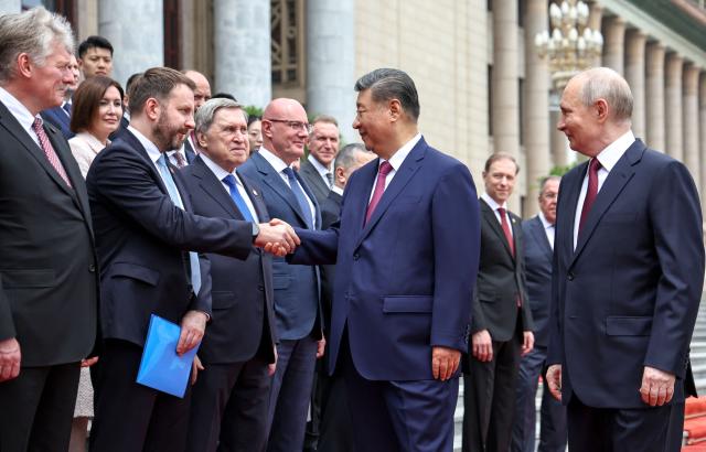 In this pool photograph distributed by the Russian state agency Sputnik, China's President Xi Jinping (C) greets members of the Russian delegation as Russia's President Vladimir Putin (R) looks on during a welcome ceremony at the Great Hall of the People in Beijing on May 20, 2026. (Photo by Alexander KAZAKOV / POOL / AFP)