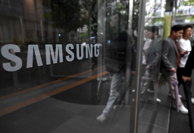 The logo of Samsung Electronics is displayed on a glass door at the company's Seocho building in Seoul on May 20, 2026. A planned strike at South Korean chip giant Samsung Electronics will go ahead from May 21, its union said, after talks on bonus payouts collapsed, raising concerns over a disruption to the country's key semiconductor industry. (Photo by Jung Yeon-je / AFP)