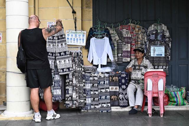A tourist looks at elephant pants at a stall outside the Grand Palace in Bangkok on May 20, 2026. Thailand is drastically cutting the length of visa-free stays for tourists from more than 90 countries in an effort to curb crime involving foreign nationals. (Photo by Lillian SUWANRUMPHA / AFP)