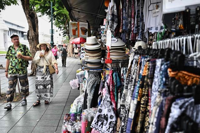 Tourists walk past souvenir shops outside the Grand Palace in Bangkok on May 20, 2026. Thailand is drastically cutting the length of visa-free stays for tourists from more than 90 countries in an effort to curb crime involving foreign nationals. (Photo by Lillian SUWANRUMPHA / AFP)