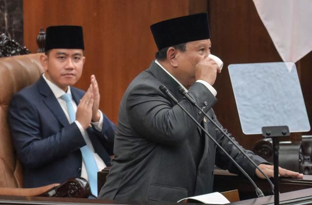 Indonesian President Prabowo Subianto (R) sips a coffee on the sidelines of his speech on the macroeconomic framework to lawmakers as Vice President Gibran Rakabuming Raka (L) looks on at the Parliament building in Jakarta on May 20, 2026. (Photo by BAY ISMOYO / AFP)