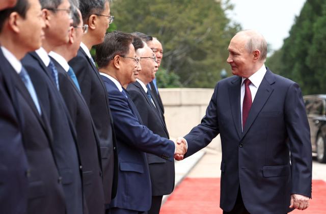 In this pool photograph distributed by the Russian state agency Sputnik, Russia's President Vladimir Putin (R) shakes hands with members of the Chinese delegation during a welcome ceremony at the Great Hall of the People in Beijing on May 20, 2026. (Photo by Alexander KAZAKOV / POOL / AFP)
