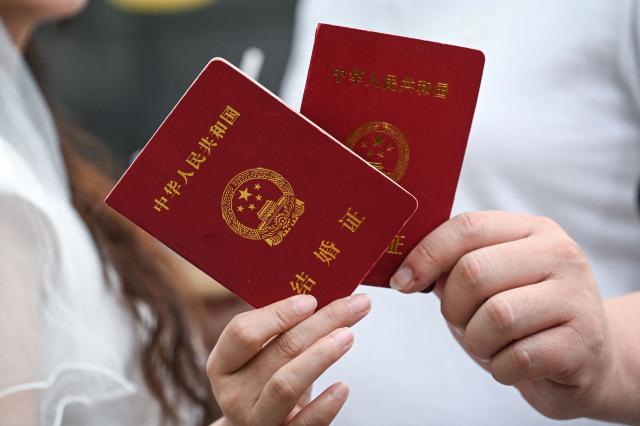 A newly-wedded couple hold their marriage certificates at a marriage registry in Shanghai on May 20, 2026, known as "520 Day", as the numbers sound like "I love you" in Chinese. (Photo by Jade GAO / AFP)