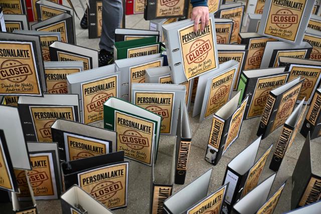 Employees demonstrate with an installation of symbolically closed personnel files in front of the venue where is taking place the annual general meeting of Germany's Commerzbank bank, on May 20, 2026 in Wiesbaden, western Germany. Commerzbank plans to fend off a hostile takeover by Italy's UniCredit with job cuts and higher profit targets. The Frankfurt-based bank announced earlier in May 2026 that it will cut a further 3,000 jobs by 2030 and raised its business targets. Lower costs and higher profits are driving up the share price, making a potential takeover more expensive. (Photo by Kirill KUDRYAVTSEV / AFP)
