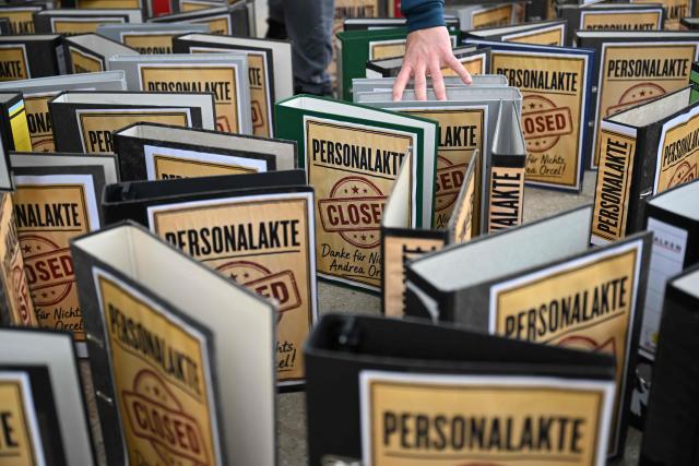Employees demonstrate with an installation of symbolically closed personnel files in front of the venue where is taking place the annual general meeting of Germany's Commerzbank bank, on May 20, 2026 in Wiesbaden, western Germany. Commerzbank plans to fend off a hostile takeover by Italy's UniCredit with job cuts and higher profit targets. The Frankfurt-based bank announced earlier in May 2026 that it will cut a further 3,000 jobs by 2030 and raised its business targets. Lower costs and higher profits are driving up the share price, making a potential takeover more expensive. (Photo by Kirill KUDRYAVTSEV / AFP)