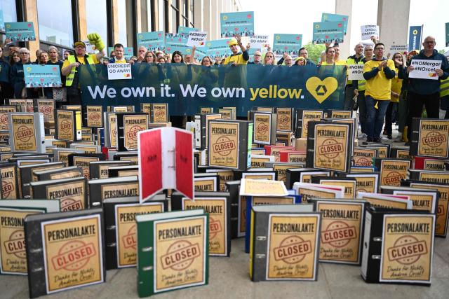 Employees demonstrate with an installation of symbolically closed personnel files in front of the venue where is taking place the annual general meeting of Germany's Commerzbank bank, on May 20, 2026 in Wiesbaden, western Germany. Commerzbank plans to fend off a hostile takeover by Italy's UniCredit with job cuts and higher profit targets. The Frankfurt-based bank announced earlier in May 2026 that it will cut a further 3,000 jobs by 2030 and raised its business targets. Lower costs and higher profits are driving up the share price, making a potential takeover more expensive. (Photo by Kirill KUDRYAVTSEV / AFP)