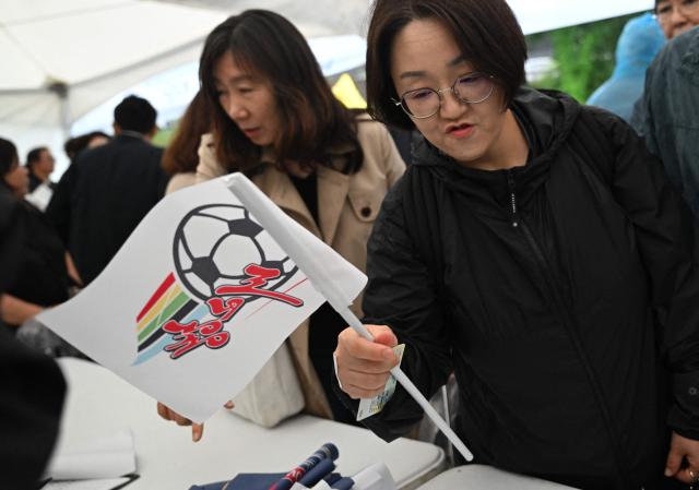 A South Korean supporter for North Korea's Naegohyang Women's FC gets a flag of the Naegohyang team at a ticket booth for the AFC Women's Champions League semi-final football match between North Korea's Naegohyang Women's FC and South Korea's Suwon FC Women in Suwon on May 20, 2026. (Photo by Jung Yeon-je / AFP)