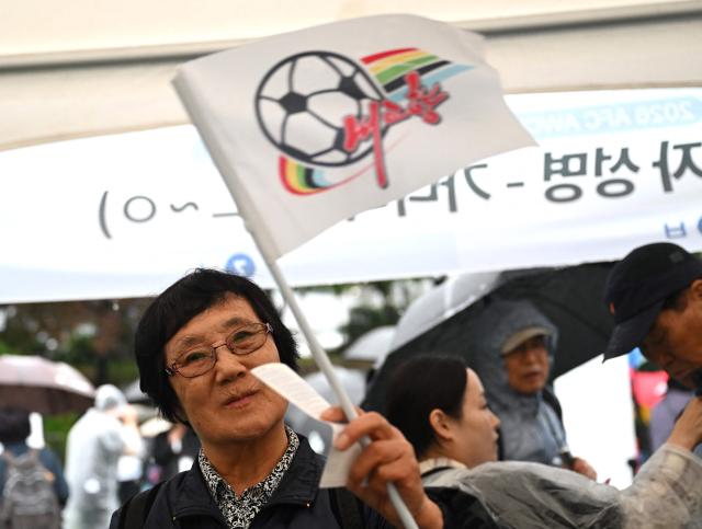 A South Korean supporter for North Korea's Naegohyang Women's FC gets a flag of the Naegohyang team at a ticket booth for the AFC Women's Champions League semi-final football match between North Korea's Naegohyang Women's FC and South Korea's Suwon FC Women in Suwon on May 20, 2026. (Photo by Jung Yeon-je / AFP)