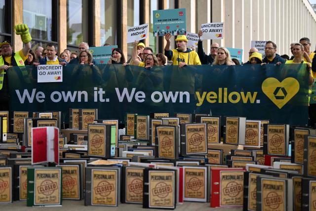 Employees demonstrate with an installation of symbolically closed personnel files in front of the venue where is taking place the annual general meeting of Germany's Commerzbank bank, on May 20, 2026 in Wiesbaden, western Germany. Commerzbank plans to fend off a hostile takeover by Italy's UniCredit with job cuts and higher profit targets. The Frankfurt-based bank announced earlier in May 2026 that it will cut a further 3,000 jobs by 2030 and raised its business targets. Lower costs and higher profits are driving up the share price, making a potential takeover more expensive. (Photo by Kirill KUDRYAVTSEV / AFP)