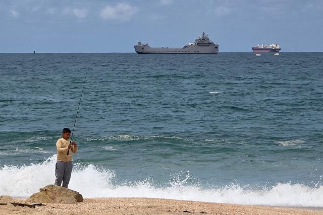 TOPSHOT - A boy fishes on the shore as an Israeli naval vessel (C) is motored towards the Israeli port of Ashdod, about 40 kilometres south of Tel Aviv, on May 20, 2026, after Israeli forces intercepted the Gaza-bound Global Sumud Flotilla. Israeli authorities have begun detaining hundreds of activists seized from a Gaza-bound flotilla at the southern port of Ashdod on May 20, a rights group said, after Israeli forces intercepted their vessels at sea. The Global Sumud Flotilla set sail from Turkey last week in the latest attempt by activists to breach Israel's blockade of the Palestinian territory, after Israeli forces intercepted a previous convoy last month. (Photo by Nir KAFRI / AFP)