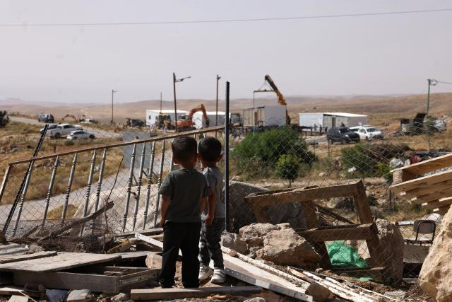 Children watch as new prefabricated Jewish outpost homes are secured into placed along a road that leads toward the Palestinian village of Umm al-Khair, wedged between the new outpost of Karmel and the Israeli settlement of Karmel, south of the town of Yatta in the southern area of the Israeli-occupied Palestinian West Bank on May 20, 2026. Alongside roughly three million Palestinians, more than 500,000 Israelis live in settlements and outposts in the West Bank, which are illegal under international law. Violence in the Palestinian West Bank, which Israel has occupied since 1967, has soared since the Hamas attack on Israel triggered the Gaza war in October 2023. (Photo by HAZEM BADER / AFP)