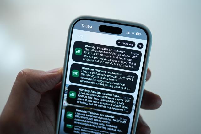 This photograph shows a person holding a mobile phone that displays a warning of a possible air raid in Vilnius on May 20, 2026. A drone alert sent by Lithuania's defence ministry to residents of the capital city Vilnius briefly brought transport to a standstill and caused people to flee to underground shelters. Alerts of this kind have been increasingly common in recent months in the Baltic states as a result of intensified Ukrainian strikes against Russian targets in the Saint Petersburg region, close to Estonia and Finland. But Wednesday's (May 20, 2026) alarm was the first in an EU and NATO member country since Russia's full-scale invasion of Ukraine began in 2022 to trigger a hunker-down alert for the population -- including the president, prime minister and MPs. (Photo by Andrei SHAULIUHA / AFP)